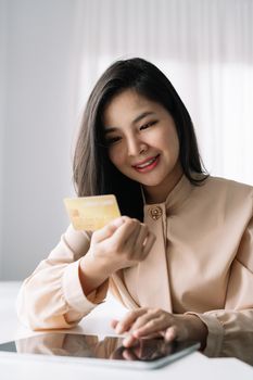 Shot of woman hold bank credit card and type on laptop, shopping online using digital tablet for buying goods or ordering online, entering bank accounts and details in online banking offer.