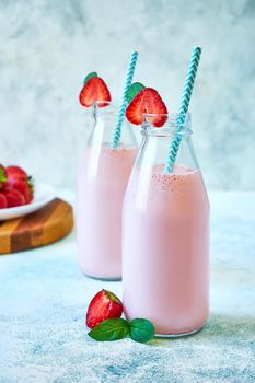 Close-up strawberry smoothie or milkshake in glass jar with berries on blue concrete background. Healthy summer drink.