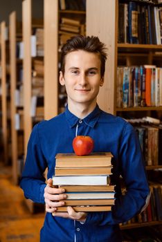 Portrait of a smiling male student with a stack of books in the library