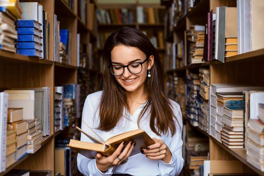 Attractive caucasian female student reading novel in literature department of college`s library