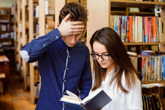 Two annoyed students at the library can't information in the book, trying to figure out it`s meaning