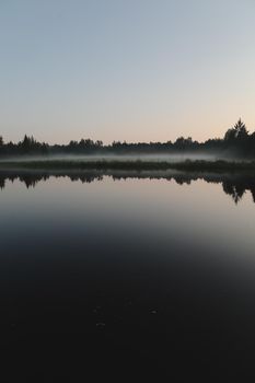summer evening twilight view on picturesque plain lake surface with reflections of sky and trees.