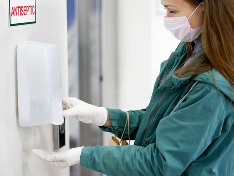 Washing hands in gloves using automatic sanitizer dispenser. Automatic sanitizer dispenser at supermarket. Coronavirus prevention. Coronavirus. Disinfectant in a shopping mall during the coronavirus epidemic.