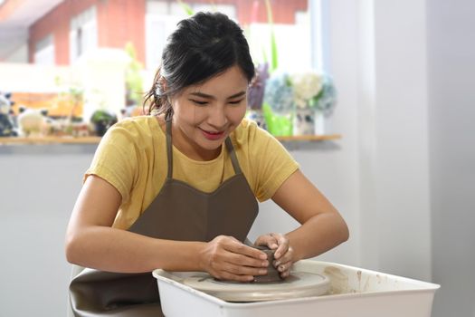 Concentrated asian woman making ceramic pot from clay in pottery workshop. Activity, handicraft, hobbies concept.