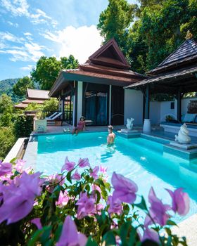 a young couple of men and women at a swimming pool during a vacation on a tropical island. man and woman in infinity pool during sunset. luxury vacation in Thailand pool of a luxury pool villa