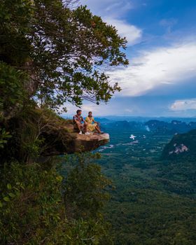 Dragon Crest mountain Krabi Thailand, a Young traveler sits on a rock that overhangs the abyss, with a beautiful landscape. Dragon Crest or Khuan Sai at Khao Ngon Nak Nature Trail in Krabi, Thailand