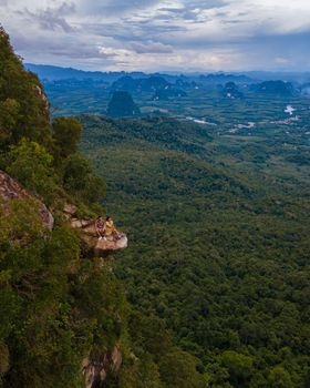 Dragon Crest mountain Krabi Thailand, a Young traveler sits on a rock that overhangs the abyss, with a beautiful landscape. Dragon Crest or Khuan Sai at Khao Ngon Nak Nature Trail in Krabi, Thailand