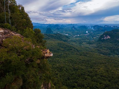 Dragon Crest mountain Krabi Thailand, a Young traveler sits on a rock that overhangs the abyss, with a beautiful landscape. Dragon Crest or Khuan Sai at Khao Ngon Nak Nature Trail in Krabi, Thailand