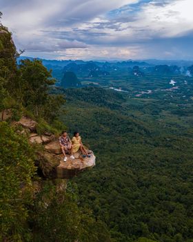 Dragon Crest mountain Krabi Thailand, a Young traveler sits on a rock that overhangs the abyss, with a beautiful landscape. Dragon Crest or Khuan Sai at Khao Ngon Nak Nature Trail in Krabi, Thailand