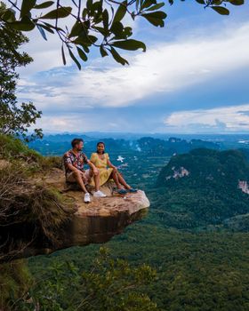 Dragon Crest mountain Krabi Thailand, a Young traveler sits on a rock that overhangs the abyss, with a beautiful landscape. Dragon Crest or Khuan Sai at Khao Ngon Nak Nature Trail in Krabi, Thailand