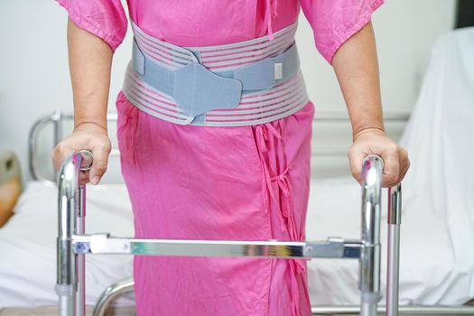 Asian senior pain back wearing elastic support belt with walker.