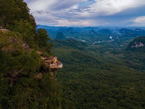 Dragon Crest mountain Krabi Thailand, a Young traveler sits on a rock that overhangs the abyss, with a beautiful landscape. Dragon Crest or Khuan Sai at Khao Ngon Nak Nature Trail in Krabi, Thailand