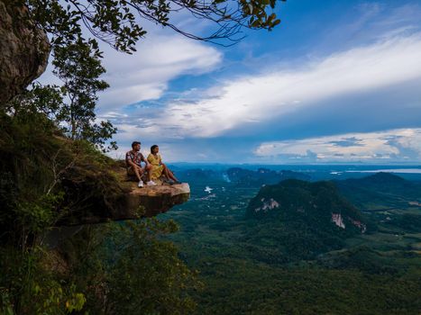 Dragon Crest mountain Krabi Thailand, a Young traveler sits on a rock that overhangs the abyss, with a beautiful landscape. Dragon Crest or Khuan Sai at Khao Ngon Nak Nature Trail in Krabi, Thailand