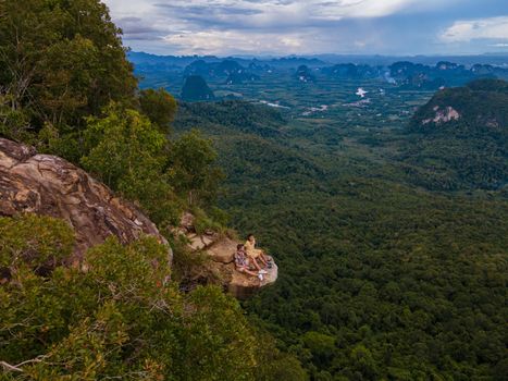 Dragon Crest mountain Krabi Thailand, a Young traveler sits on a rock that overhangs the abyss, with a beautiful landscape. Dragon Crest or Khuan Sai at Khao Ngon Nak Nature Trail in Krabi, Thailand