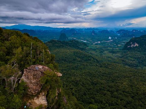 Dragon Crest mountain Krabi Thailand, a Young traveler sits on a rock that overhangs the abyss, with a beautiful landscape. Dragon Crest or Khuan Sai at Khao Ngon Nak Nature Trail in Krabi, Thailand