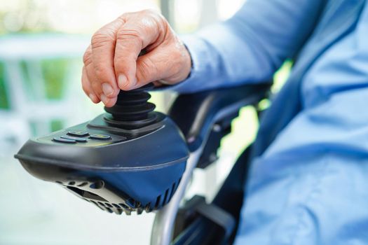 Asian elderly woman disability patient sitting on electric wheelchair in park, medical concept.