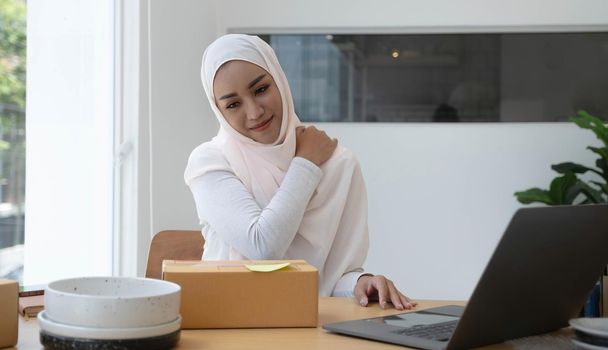 A portrait of a cute smiling teenage Muslim woman wearing a light pink hijab sits in a chair and closes her eyes to take a few naps after exhausting her hard work. overtime concept.