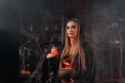 Halloween, witch use magic book and cauldron prepare poison or love potion. Black magic occult female wizard in dark room with smoke, spider web. Necromancer cooking magic potion. Close up