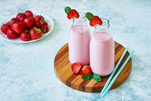 Strawberry smoothie or milkshake in glass jar with berries on wooden board on blue concrete background. Healthy summer drink