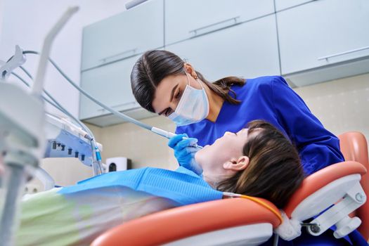 Doctor dentist treats teeth to a young teenage female patient. Real process of treatment, dental care, orthodontics, therapy, health care, dentistry concept