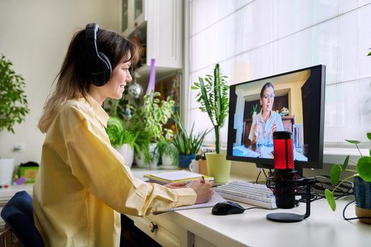 Teenage female student studying online at home, female in headphones with notebook talking to teacher by video, using computer. Chat call conference, e-learning college high school, technology concept