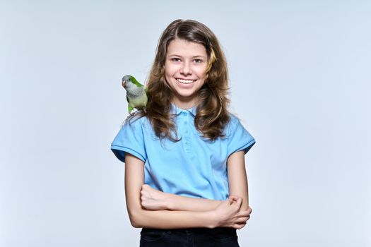 Smiling child girl with pet green quaker parrot looking at camera on light studio background. Animals, bird owner, childhood, child and pet friendship concept
