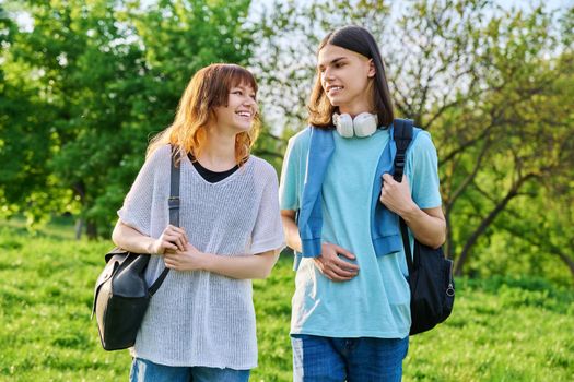 Portrait of teenage young guy and girl students outdoor. Couple of young people with backpacks, on green lawn of campus. Teenagers, lifestyle, joy, friendship, education concept