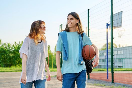 Young teenage male female students with backpacks ball walking outdoor near basketball playground court. Youth, active healthy lifestyle, education, college, high school, urban sport concept