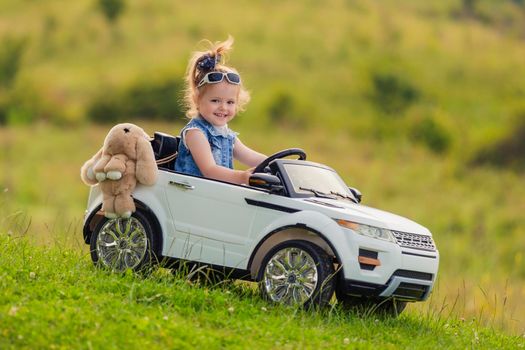 little girl rides on a children's car on a green lawn