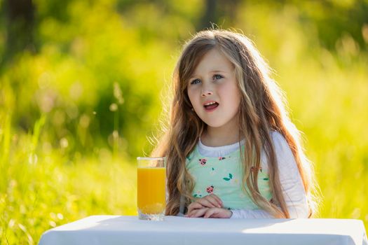 little girl in nature with a glass of orange juice