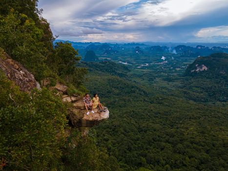 Dragon Crest mountain Krabi Thailand, a Young traveler sits on a rock that overhangs the abyss, with a beautiful landscape. Dragon Crest or Khuan Sai at Khao Ngon Nak Nature Trail in Krabi, Thailand