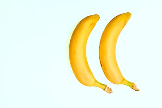 a long curved fruit which grows in clusters and has soft pulpy flesh and yellow skin when ripe.Two ripe bananas on a pale green background.