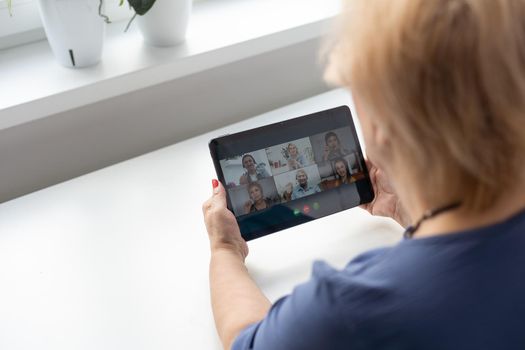 Merry mature middle-aged woman spends leisure time at home using a digital tablet. Cheerful modern senior lady holds computer, watching funny movies and laughs. Leisure and technology concept