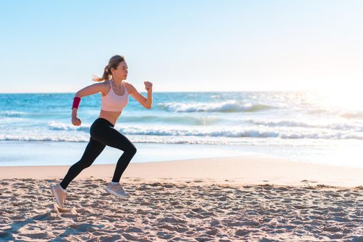 Sporty blonde woman running ocean beach. Young caucasian female exercising outdoors running seashore. Concept of healthy running and outdoors exercise. Active, sporty athlete jogging. Summer active