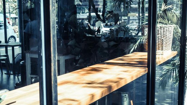 Wooden table in front of the blur background with the shadow of tree flower and window.coffee shop. Lifestyle nature evironment.