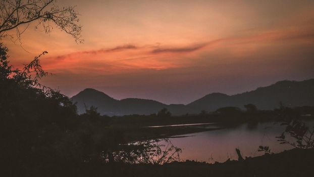 Landscape with orange and purple at sunset  silhouettes of mountains, hills and forest lake