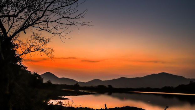 Landscape with orange and purple at sunset  silhouettes of mountains, hills and forest lake