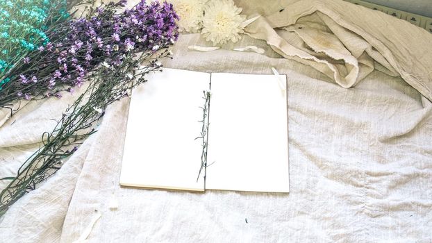 Blank white paper notebook and flower decoration. Greeting card on a white natural; linen background. Top view. Copy space.