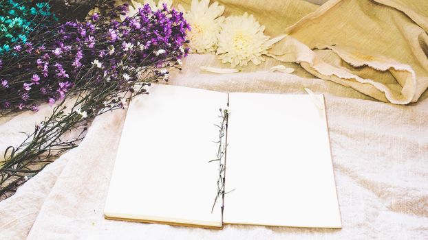 Blank white paper notebook and flower decoration. Greeting card on a white natural; linen background. Top view. Copy space.