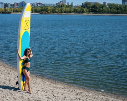 Caucasian woman walks along the beach and carries a sup board on the river in the city. Summer sport