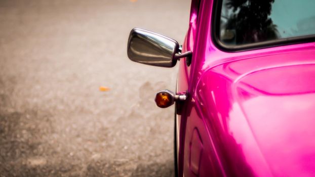 Side mirror and window of beautiful vintage pink car over blur background