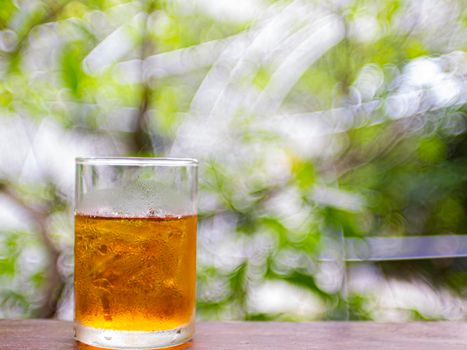 Glass of ice tea on wooden table blur green nature background