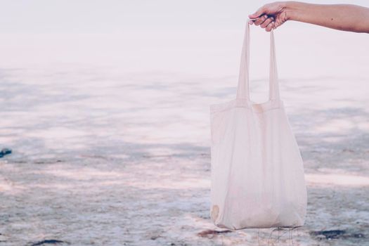 White blank cotton eco tote. Design mockup. Holding blank canvas tote bag, design mockup. Handmade shopping tote bag for girls. Beach background. Summer idea