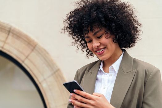 portrait of a young woman with curly hair smiling happy typing a message with her mobile phone, concept of youth and technology, copy space for text