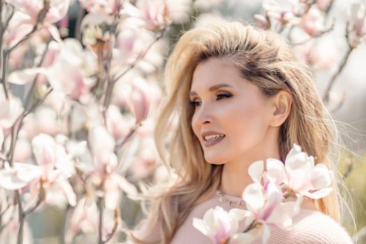 Portrait of a beautiful happy middle aged woman enjoying the smell in a blooming spring garden. Beautiful magnolia bushes, large flowers