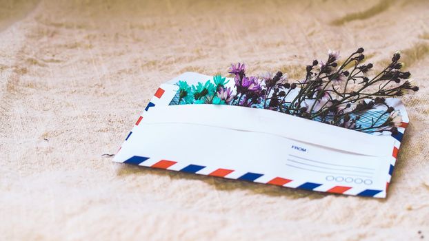 Opened envelope with small little flowers arrangements on linen background, top view. Festive greeting concept.