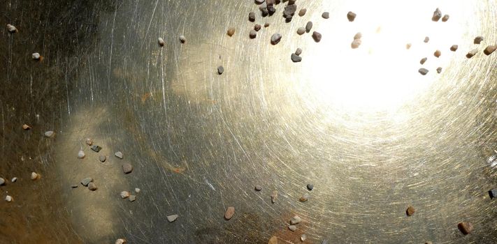 The sun reflects in a brass plate in the center of a spiritual well. The plate is full of scratches and some gravel has fallen on it. Meant as background. Seen in Frenswegen, Germany