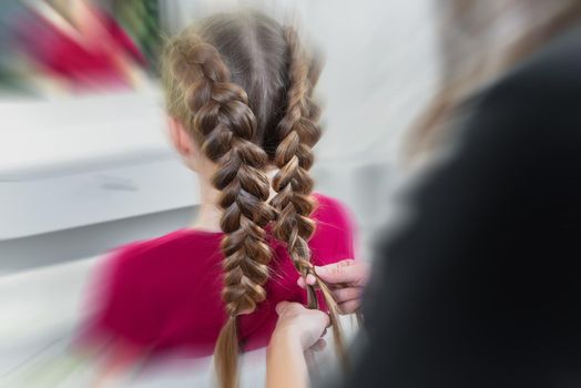 Hairdresser weaves a braid to a preteen blond girl