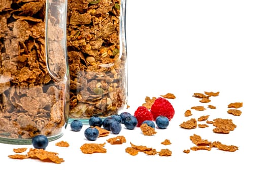 Isolate muesli. Dry muesli flakes with raspberries and blueberries lie on an isolated white background. Breakfast cereals in a glass jar on a white background