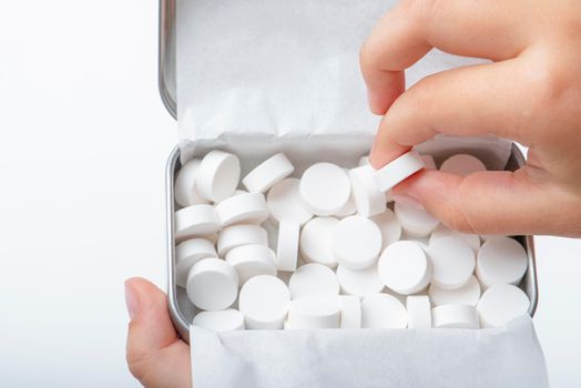 Mint candies on a white background. White mint candies in an open tin box. Fresh breath or bad breath concept. The child takes one lollipop out of the box with his hand